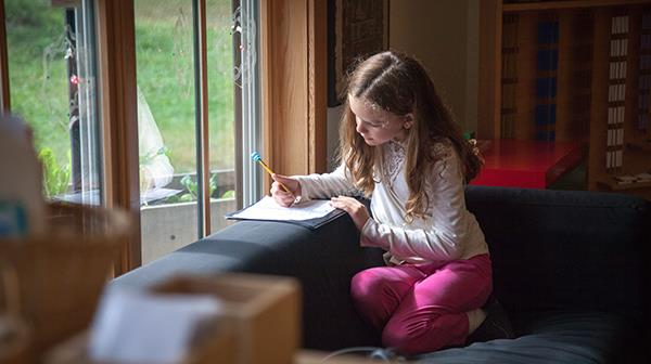 Elementary child sitting on a couch by a window with a notebook