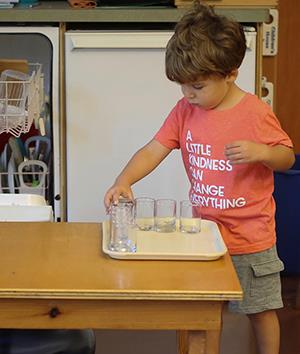 pre-school child emptying the dishwasher and putting small glasses on a tray