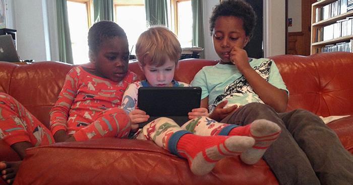 Three preschool and elementary children sitting on a couch looking at an ipad
