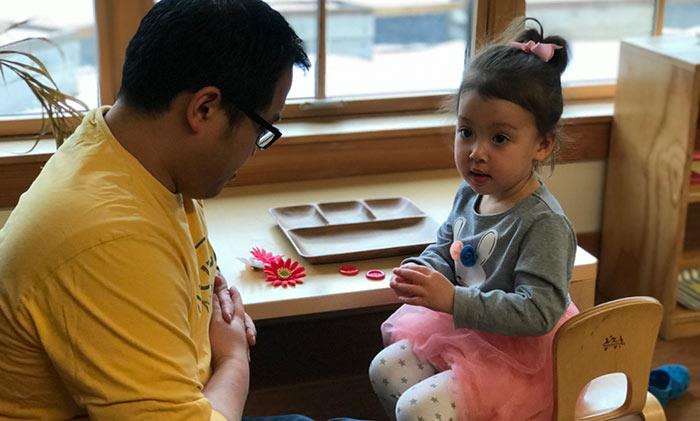 preschool child sitting at small table talking with an adult