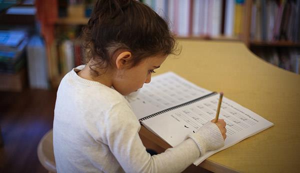 first grade child writing in a cursive workbook at small table