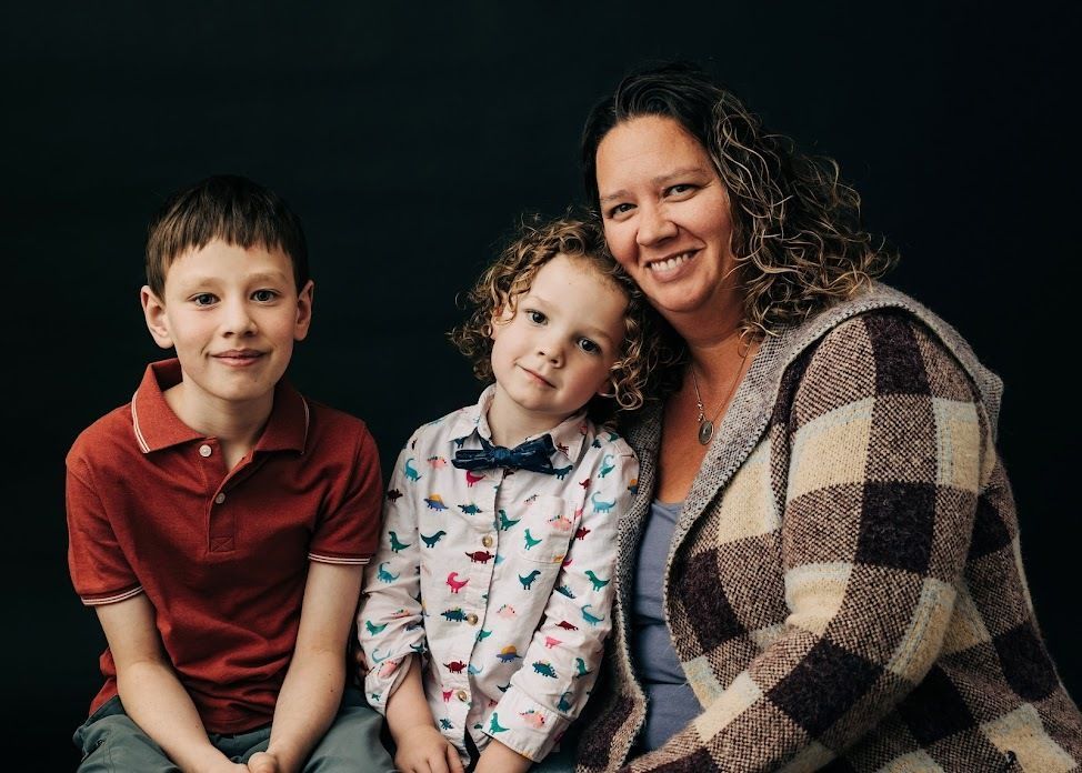 Smiling parent sitting with two children against a dark background