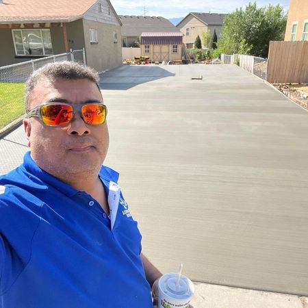 A man wearing sunglasses is taking a selfie in front of a concrete driveway.