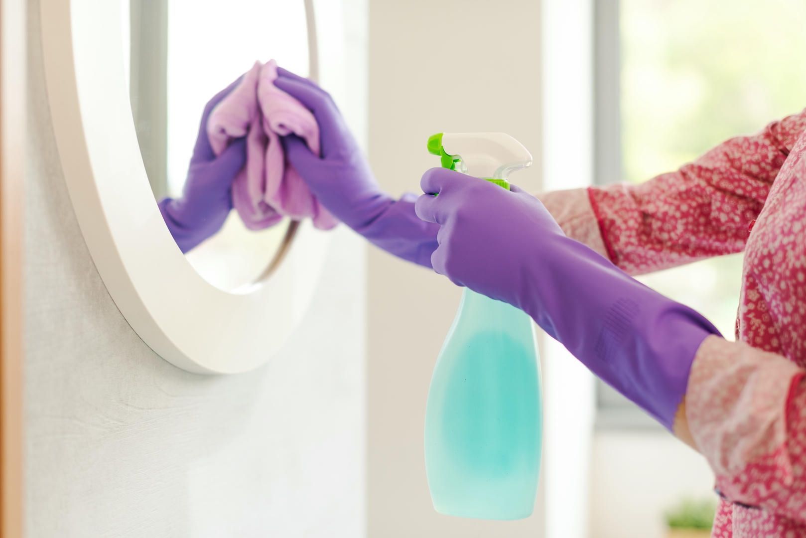 A woman in purple gloves is cleaning a mirror with a cloth.