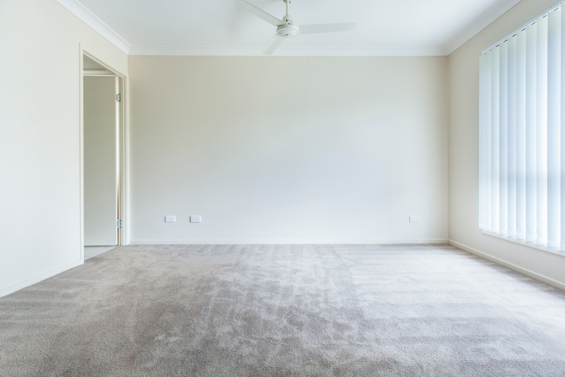 An empty living room with a ceiling fan and blinds.