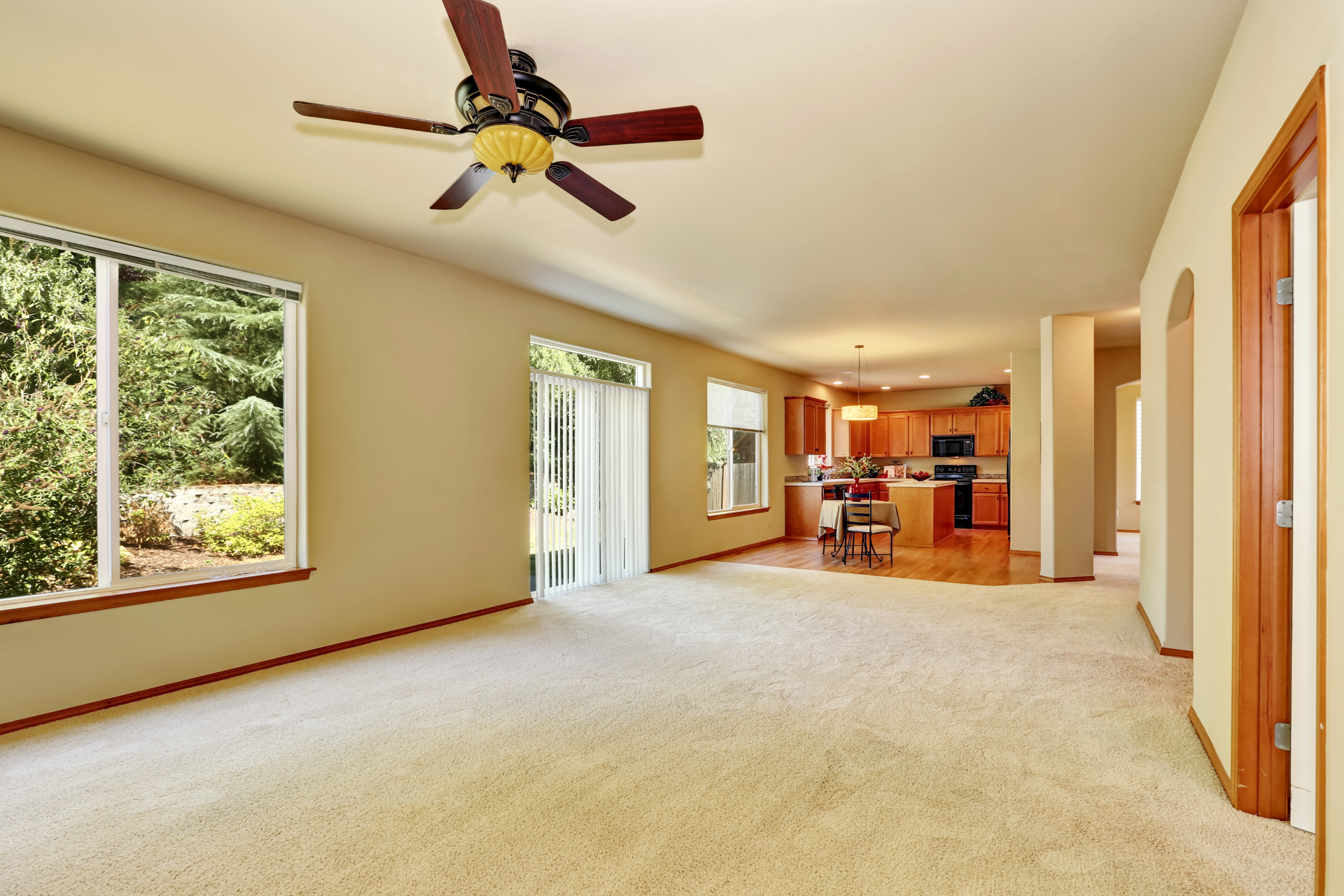 An empty living room with a ceiling fan and sliding glass doors