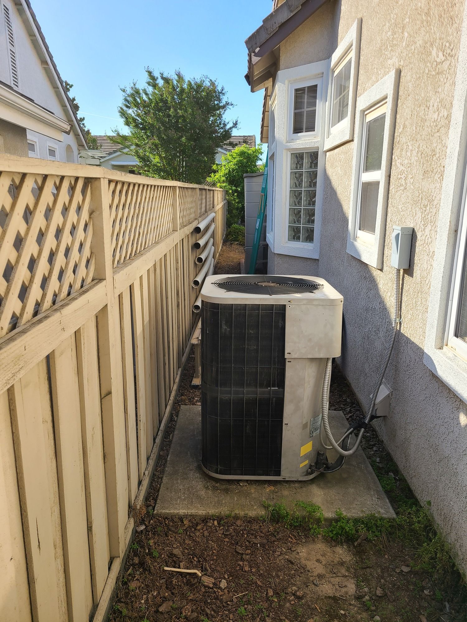 AC unit next to a house and fence on a concrete slab outdoors.