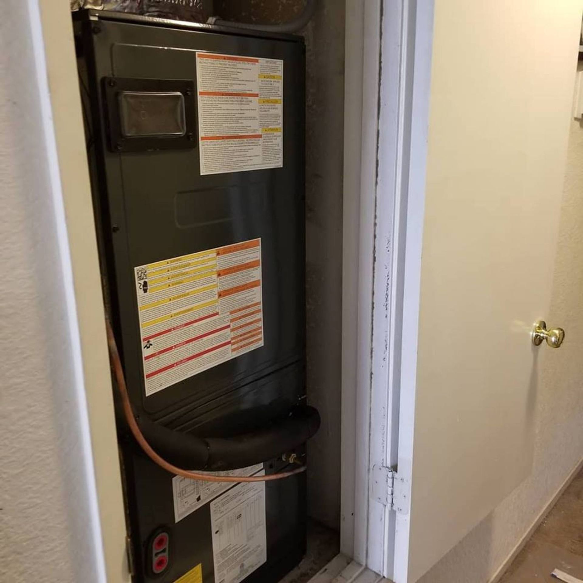 Furnace in a closet with attached ductwork and warning labels.