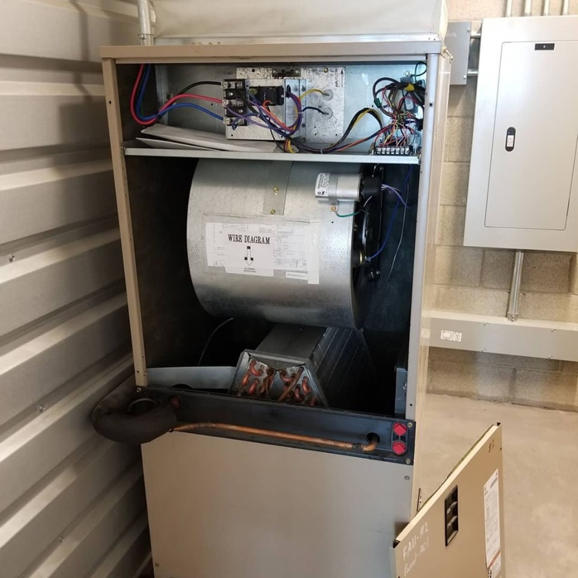 Open furnace unit with visible components, wires, and blower fan in a utility space.