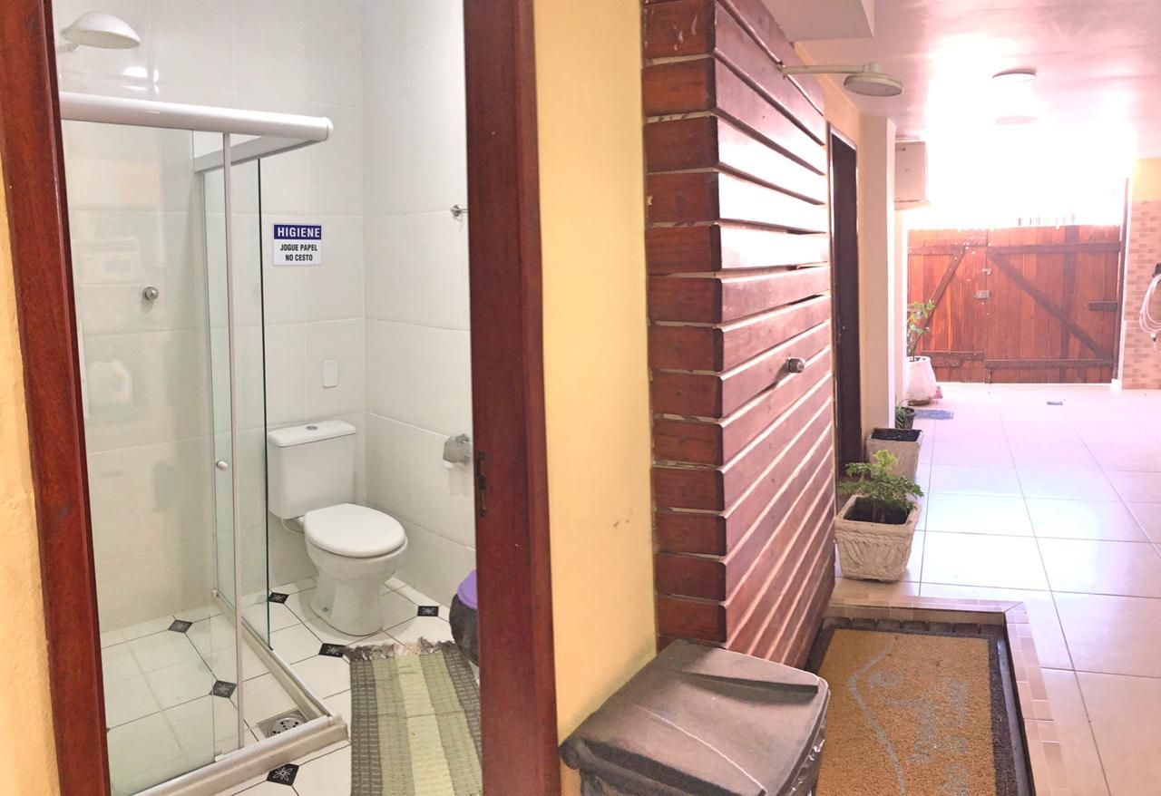 Banheiro com chuveiro, vaso sanitário e acesso à área externa por porta de madeira.
