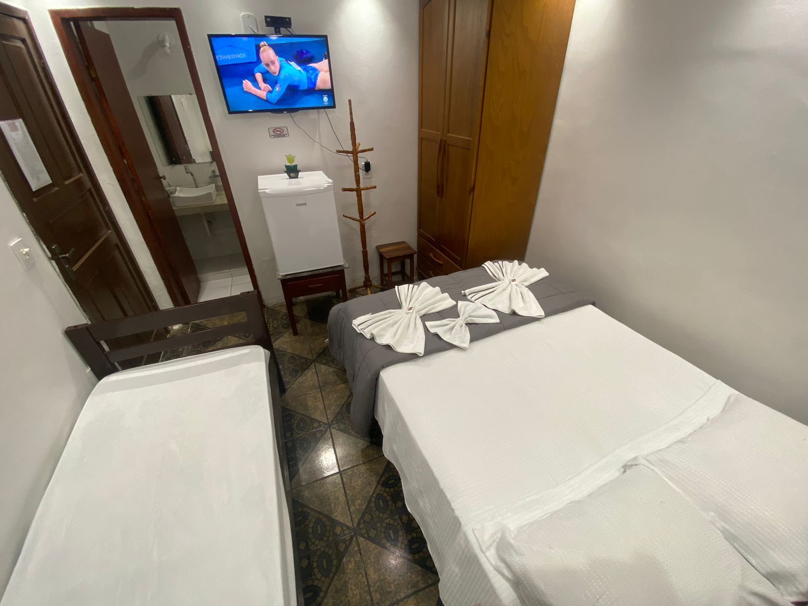 Quarto de hotel pequeno com duas camas, TV, guarda-roupa e porta para o banheiro.