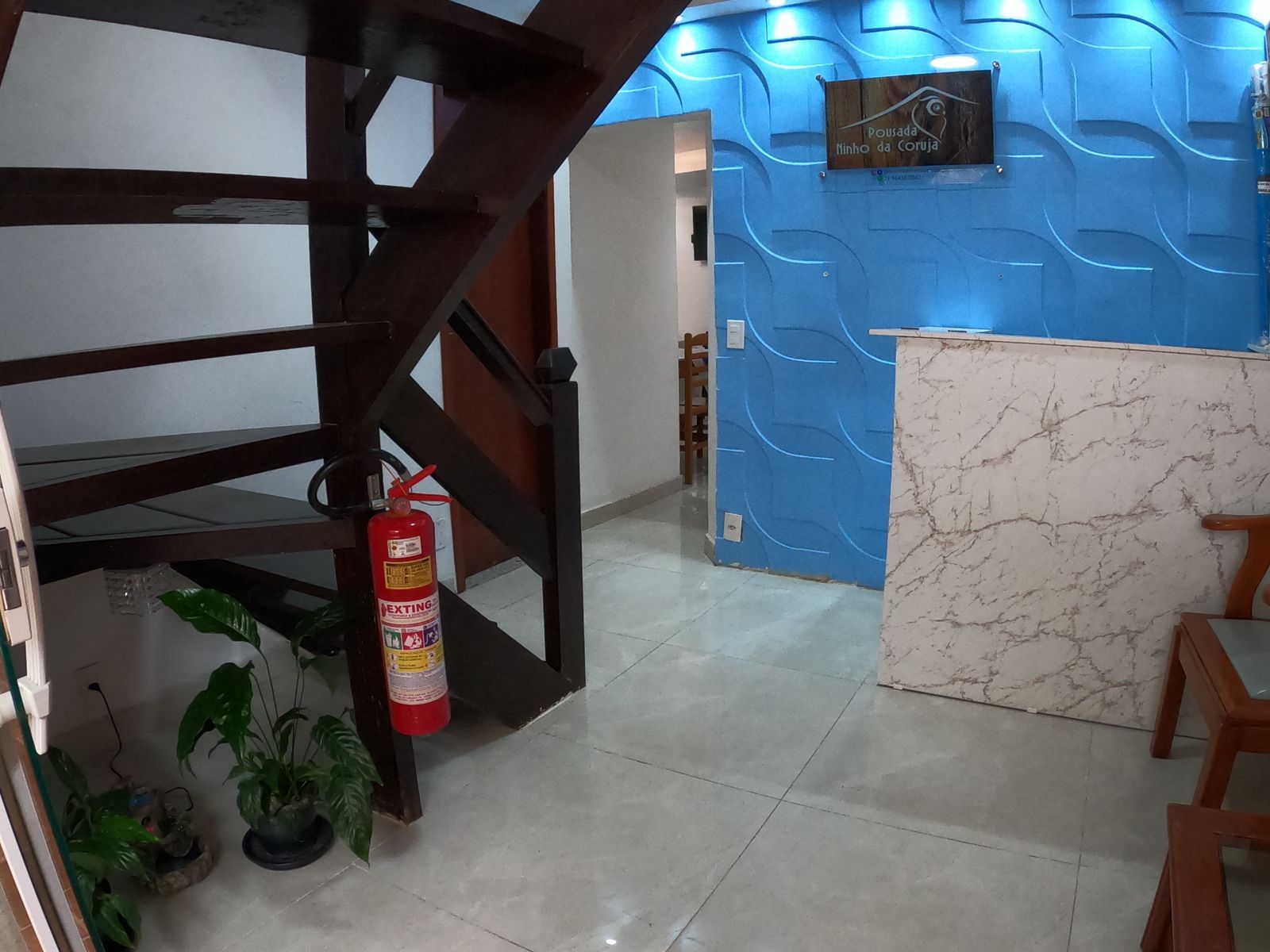 Escada ao lado da recepção com parede texturizada em azul. Um extintor de incêndio está fixado na parede.