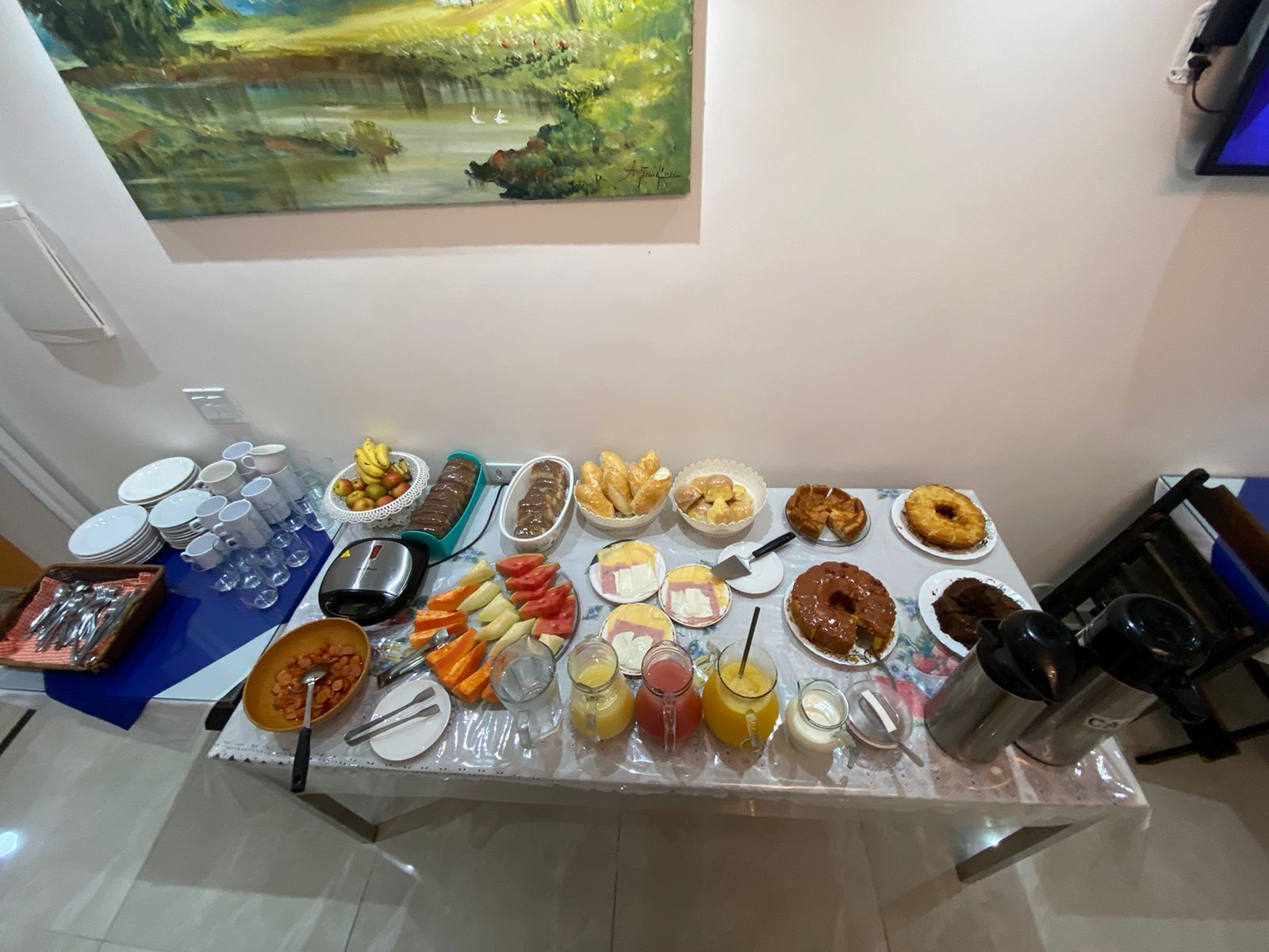 Buffet de café da manhã servido em uma mesa com frutas, doces e bebidas.