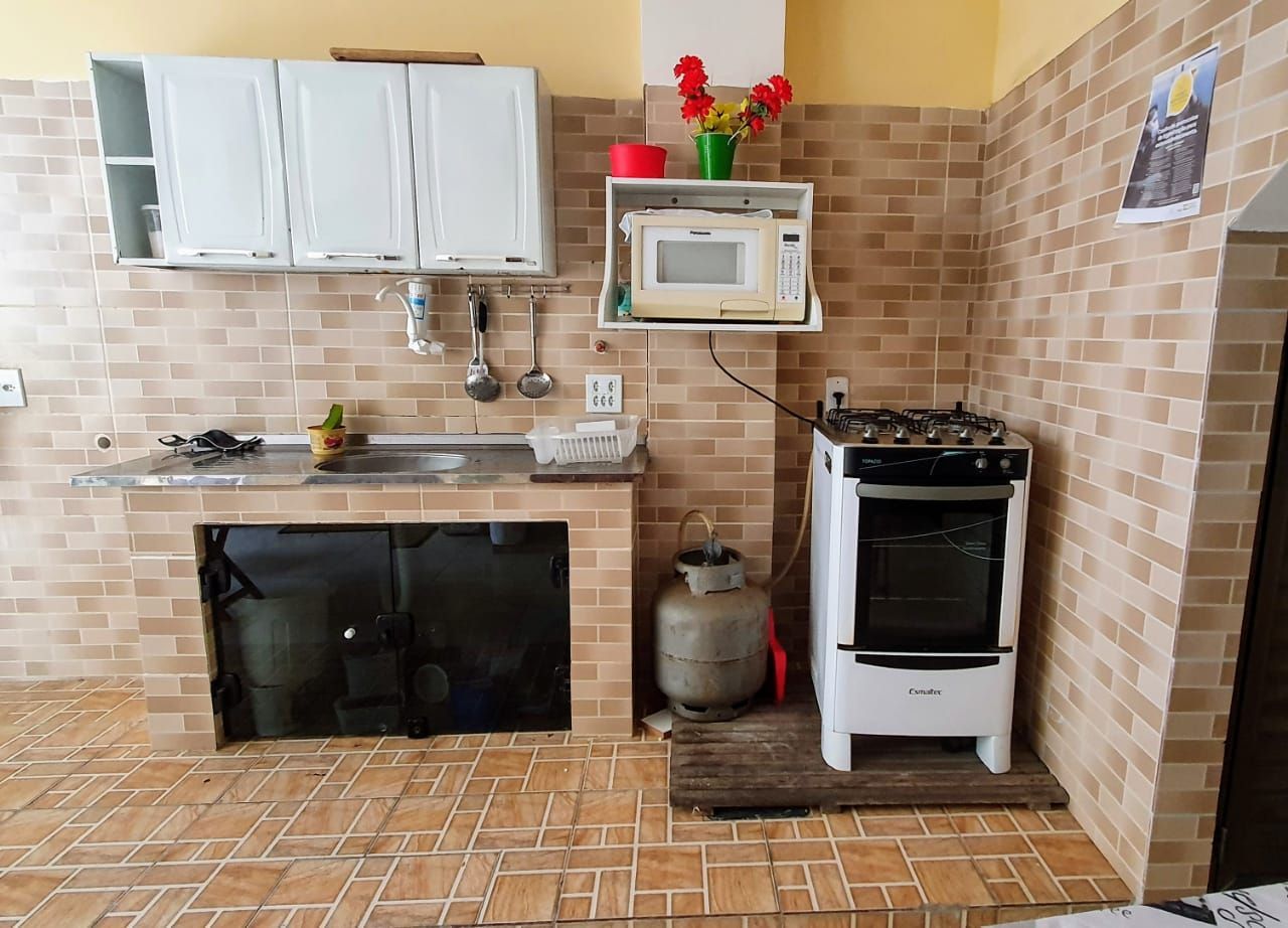 Cozinha com armários brancos, fogão, micro-ondas e azulejos com estampa de tijolos.