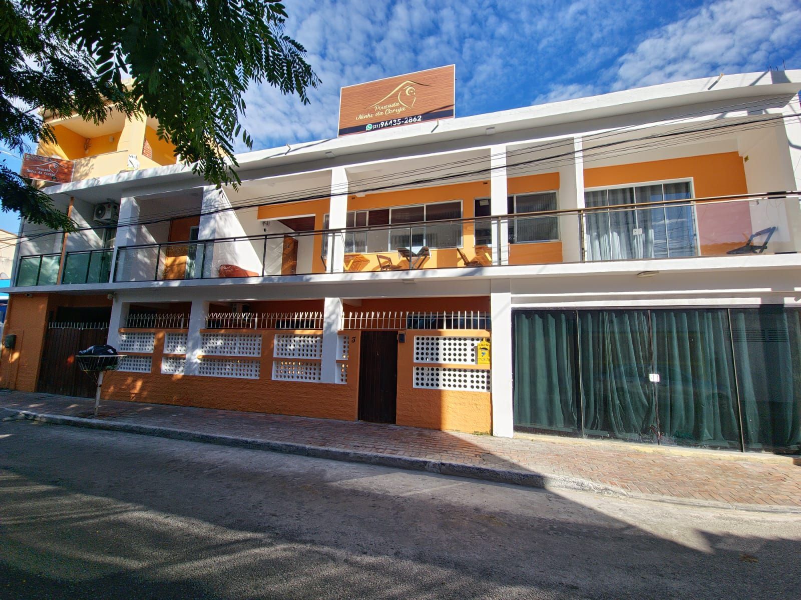 Prédio de dois andares com fachada laranja e branca, varandas e porta de garagem verde fechada.