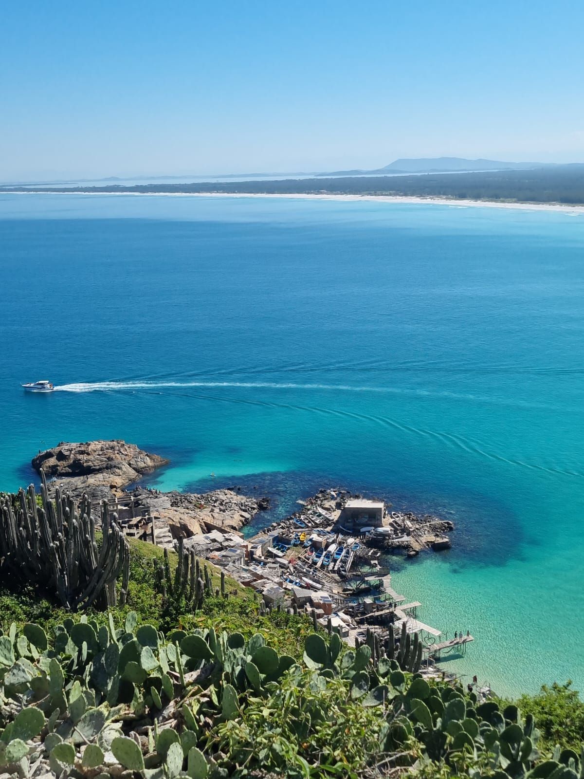 Litoral oceânico de um azul brilhante com costa rochosa, água turquesa e praia ao longe.