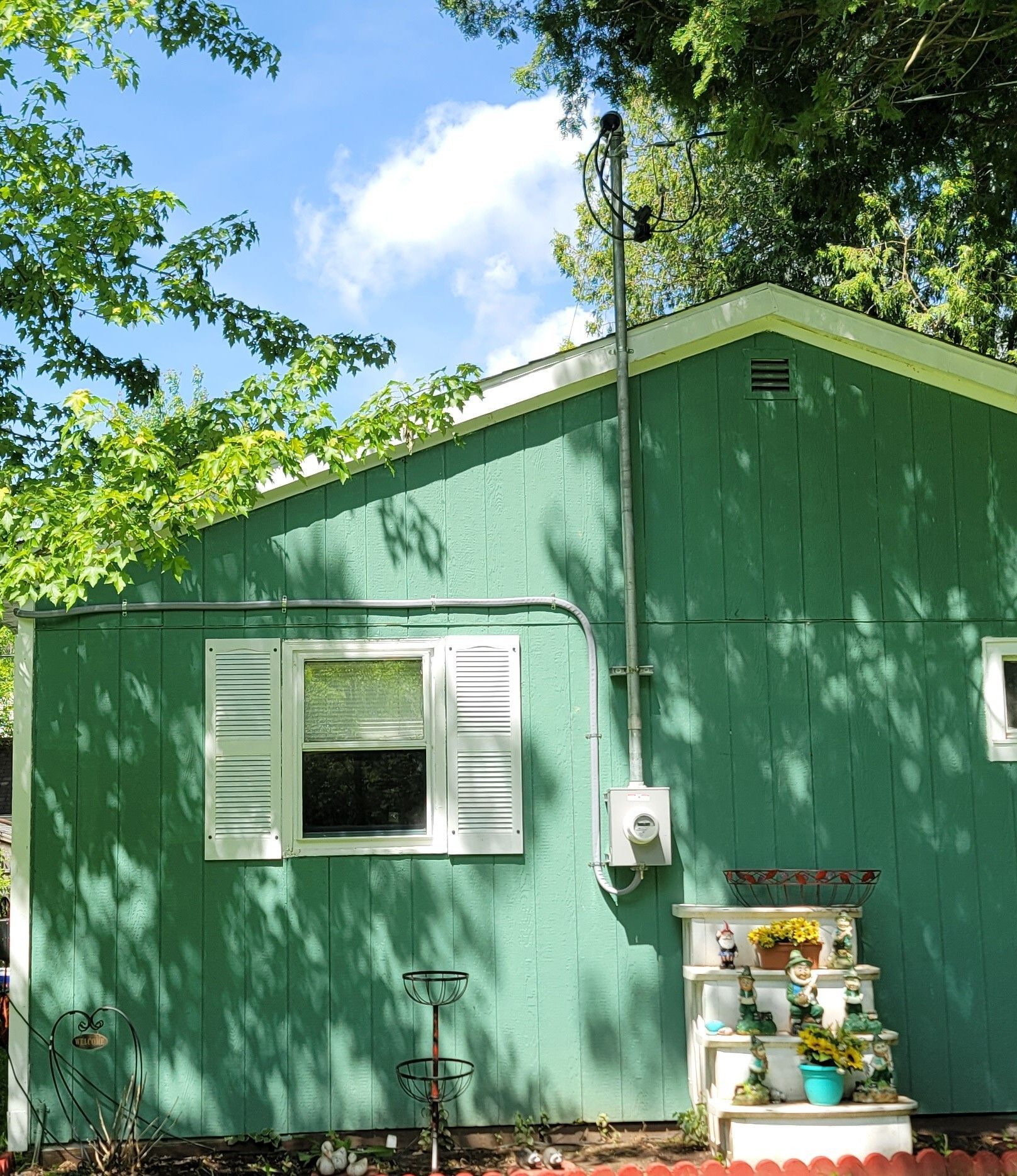 Green house with electrical conduit running up side; window, display shelf, and sky visible.