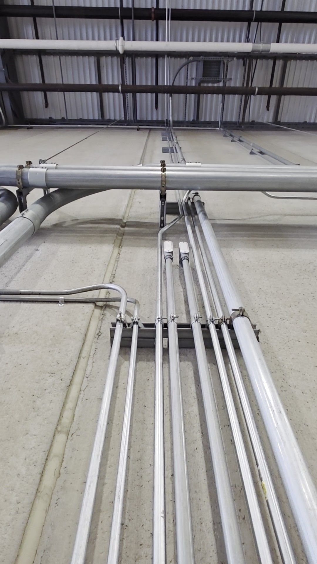 Gray pipes mounted on a concrete wall, running vertically and horizontally, with metal brackets.