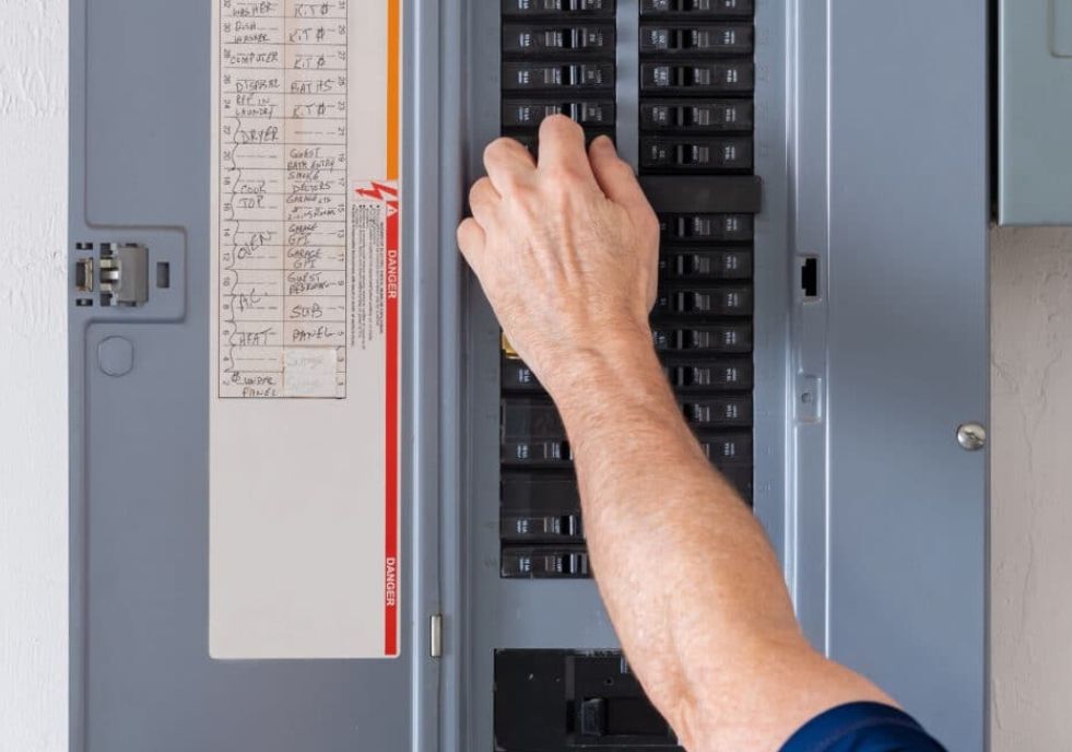 A person's hand flipping a circuit breaker on a gray electrical panel.