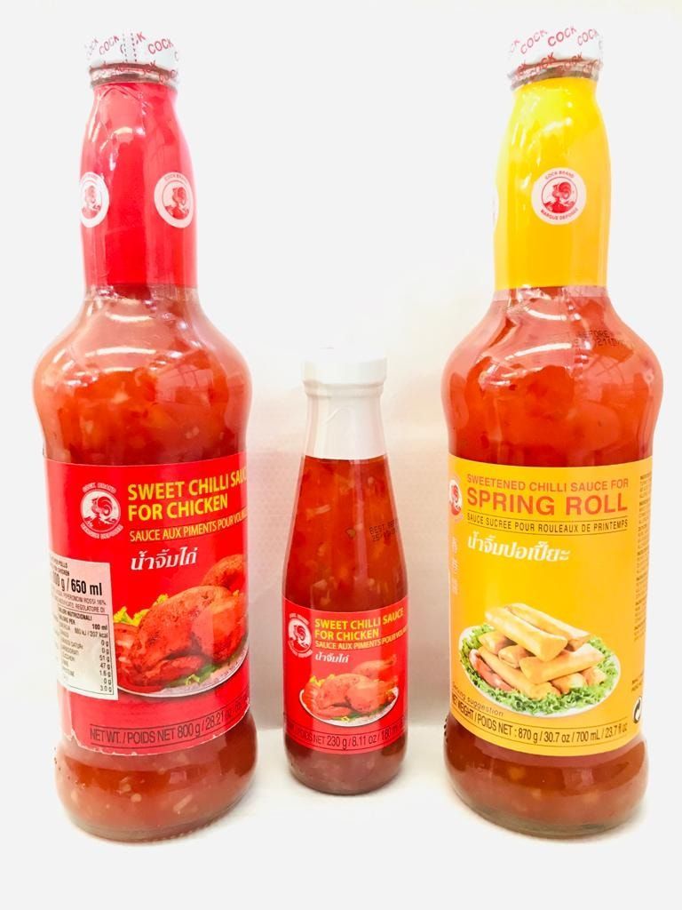Tre bottiglie di salsa thailandese, con etichette rosse e gialle, disposte su uno sfondo bianco.