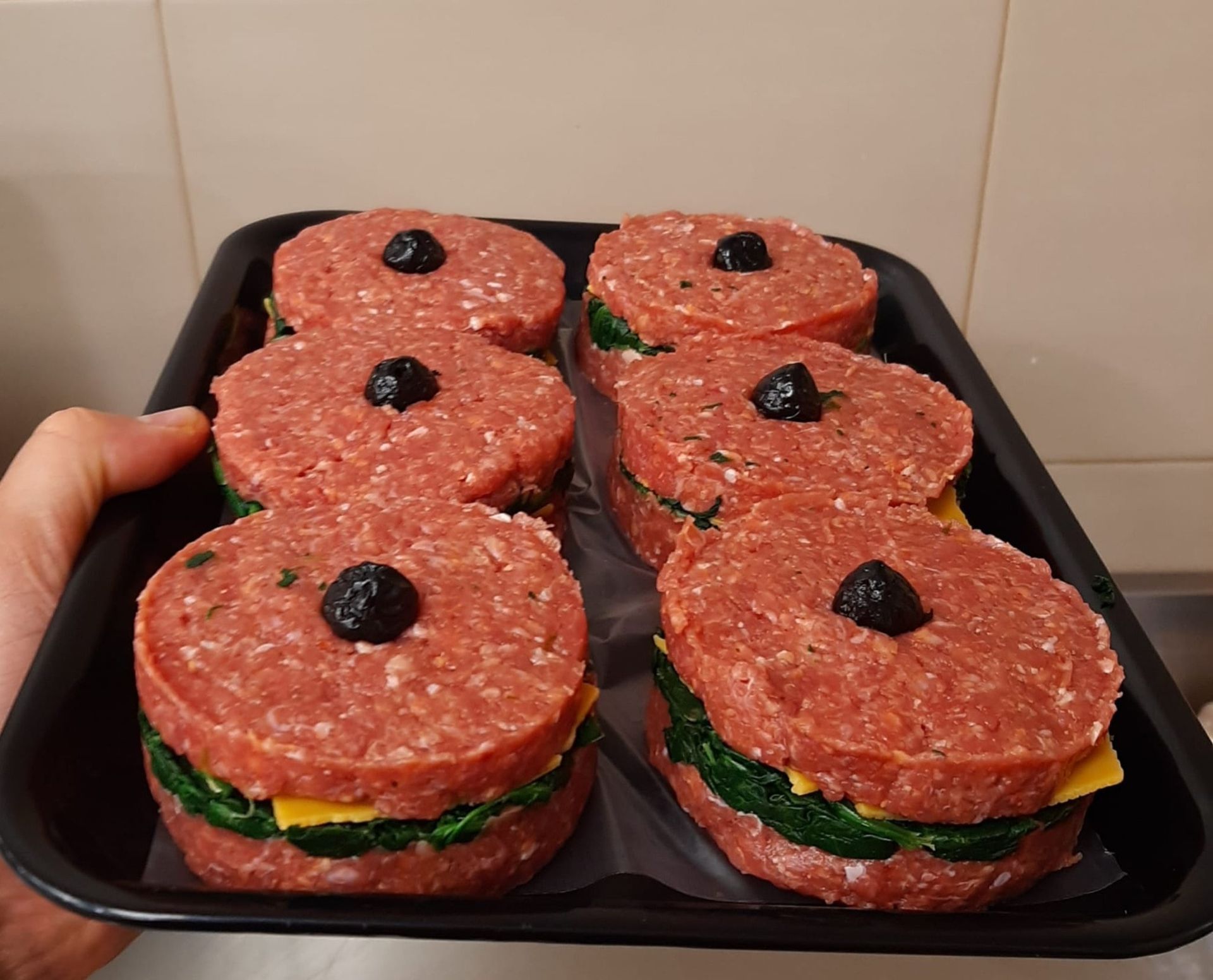 Un vassoio di tramezzini aperti al salame, guarniti con olive nere, tenuto in mano in una cucina.