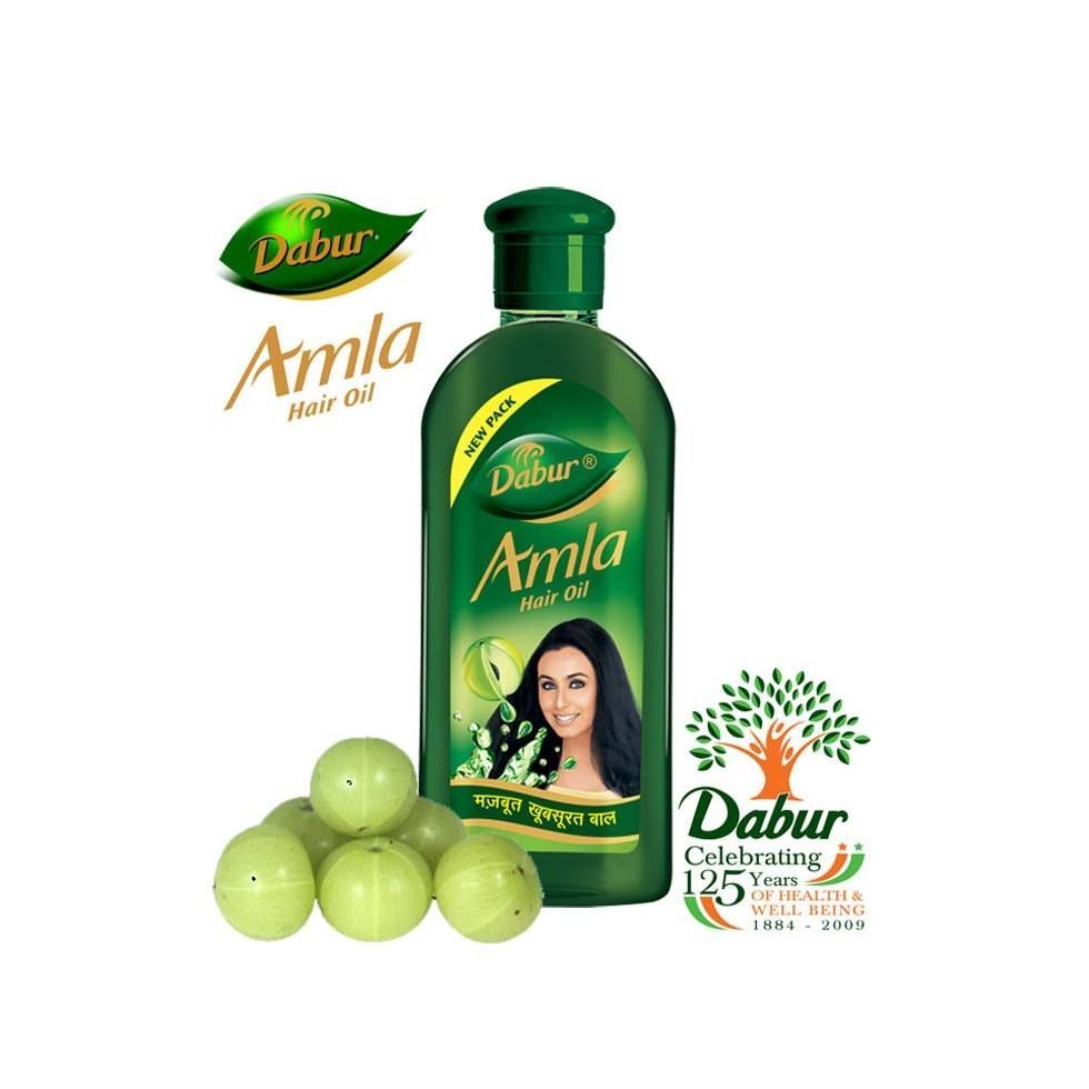 Flacone di olio per capelli Dabur Amla con frutti di amla su sfondo bianco e un'etichetta con una donna.