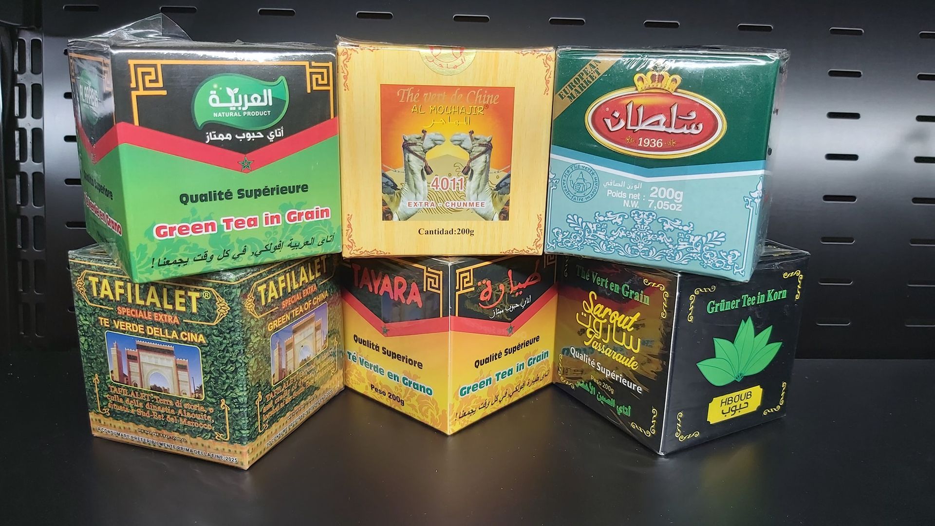 Scatole di tè colorate assortite, con confezioni in arabo e in inglese, esposte su uno scaffale nero.