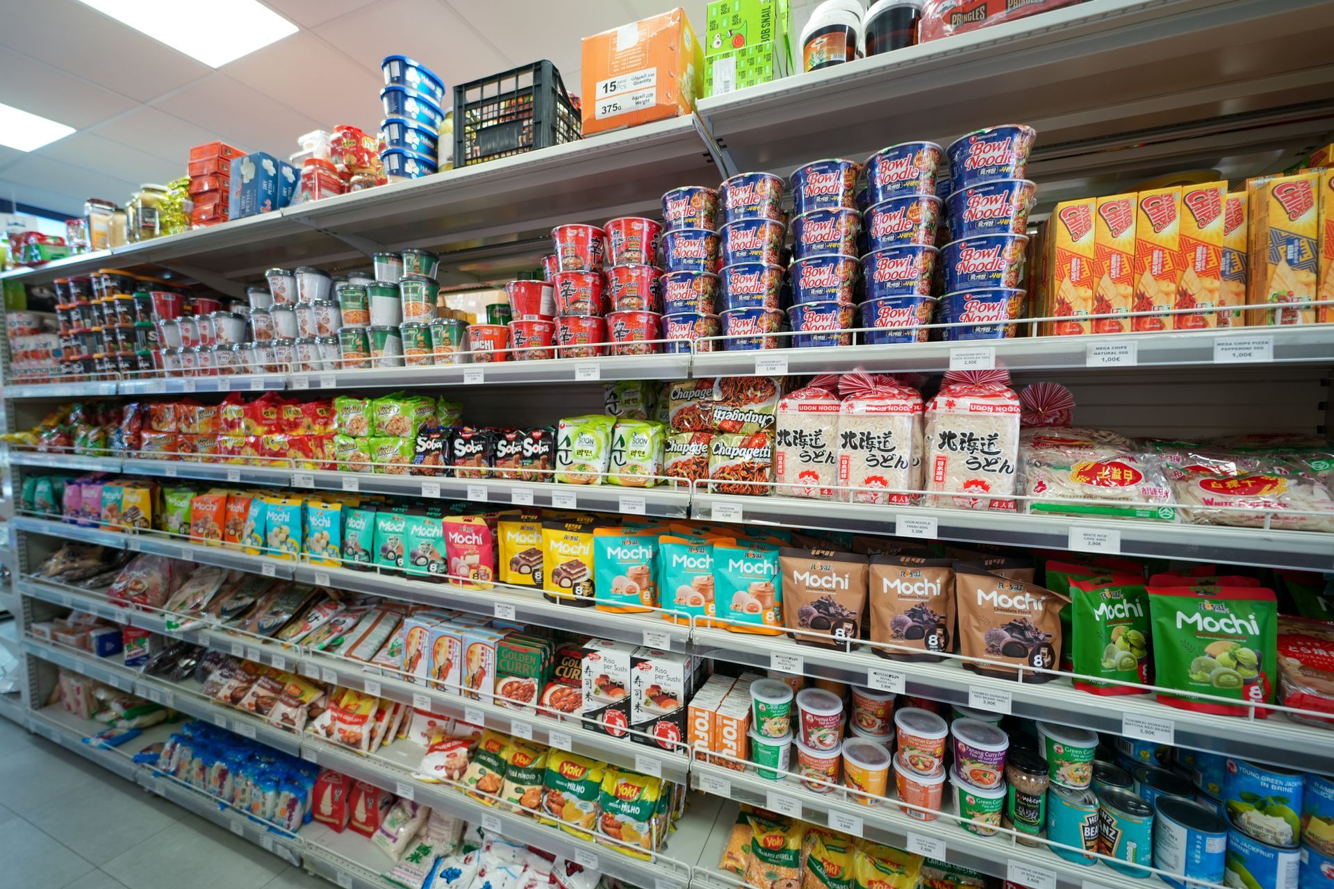 Corridoio del supermercato pieno di coloratissime conserve, snack e alimenti confezionati disposti su scaffali di metallo.