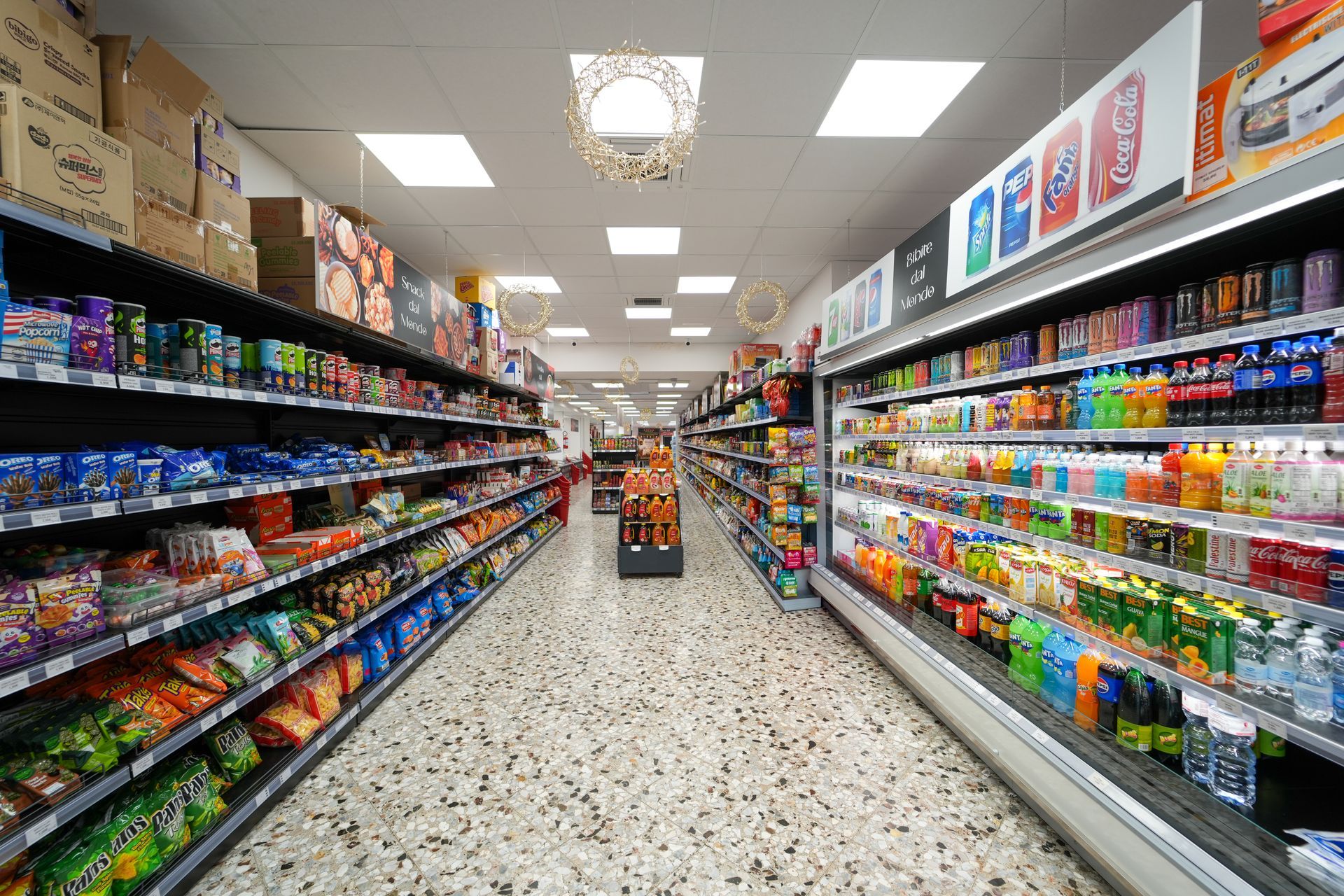 Corridoio di un supermercato con scaffali pieni di snack e bevande colorate sotto luci intense del soffitto.