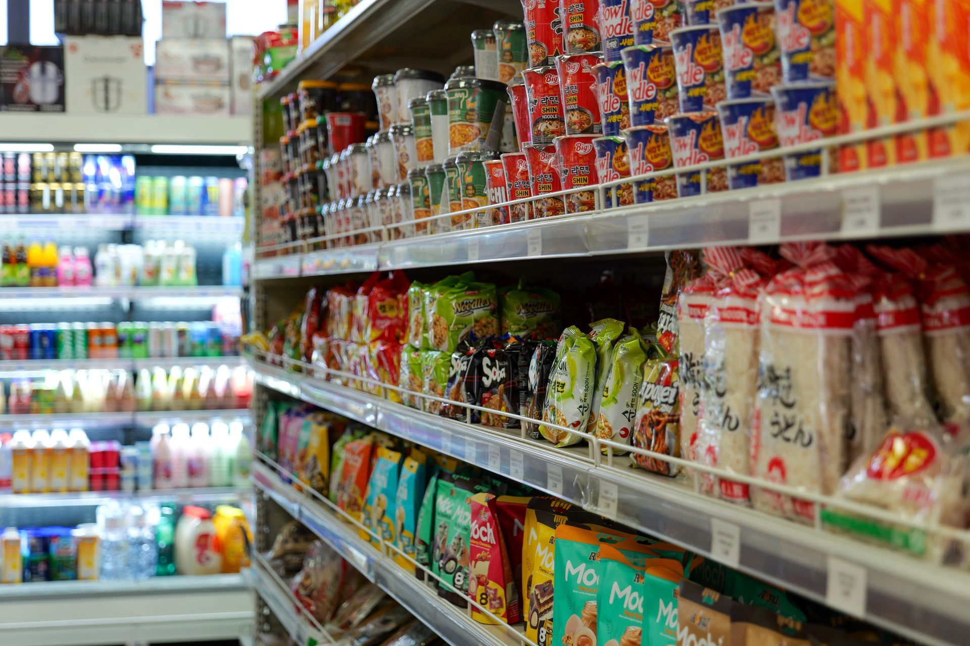 Un corridoio di un minimarket con scaffali pieni di snack e bevande confezionati e colorati.
