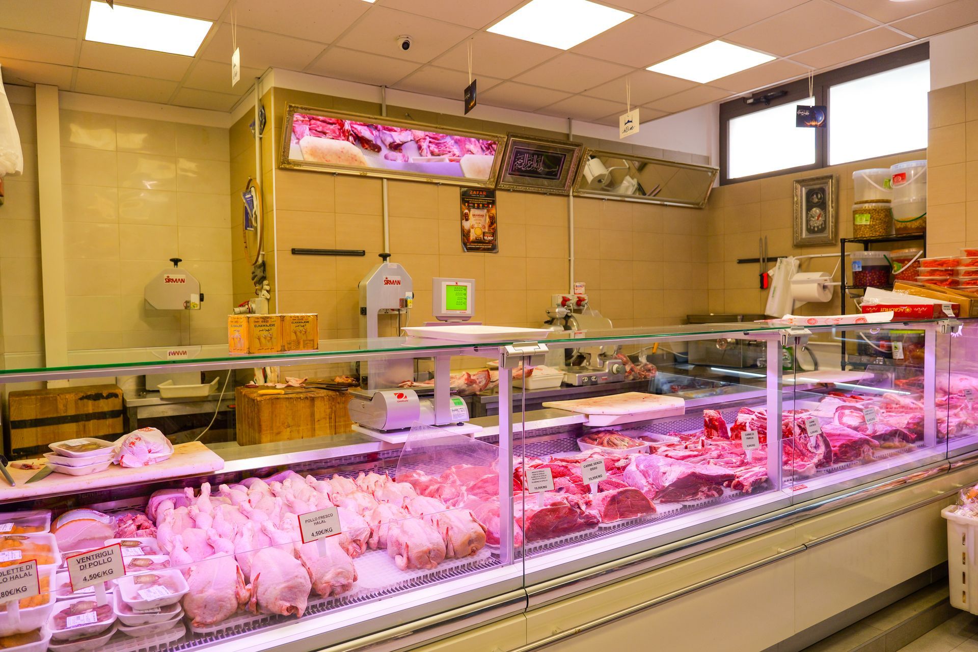 Vetrina espositiva di una macelleria con vari tagli di carne cruda sotto luci intense.