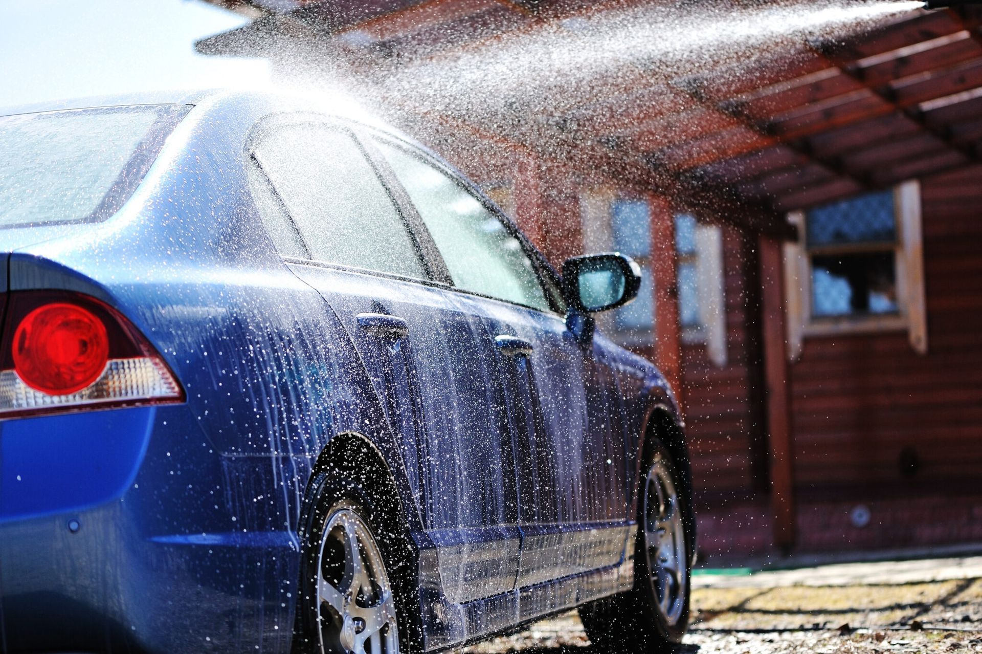 A blue car is being washed in front of a house.