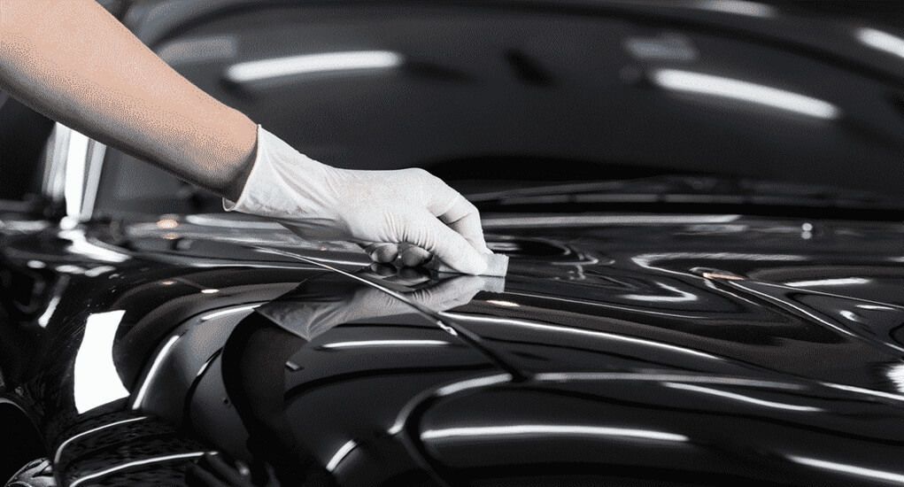 A person is polishing the hood of a black car.