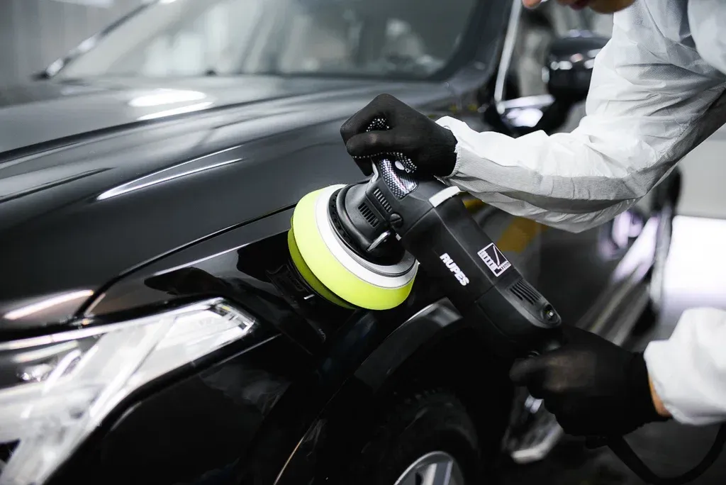 A man is polishing a black car with a machine.