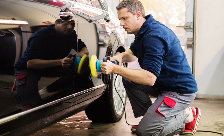 A man is polishing a car with a machine in a garage.