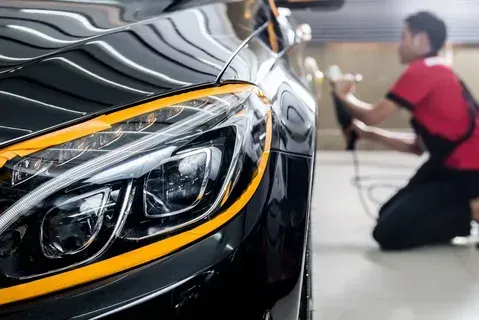 A man is polishing a black car in a garage.