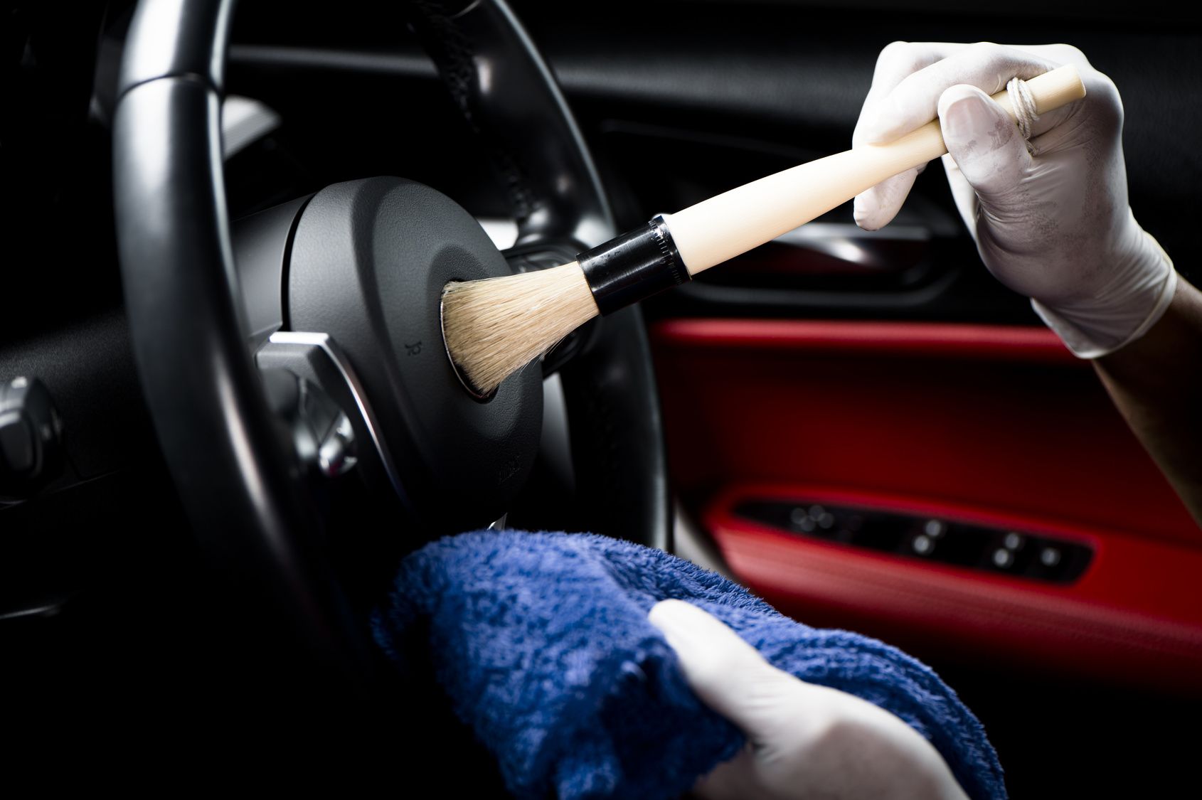 A person is cleaning the steering wheel of a car with a brush.