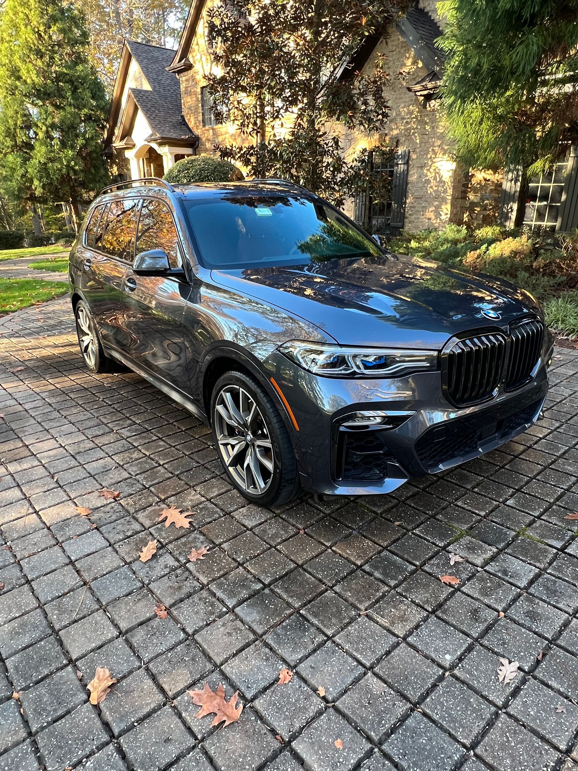 Dark blue BMW X7 SUV parked on a brick driveway in front of a house.