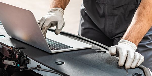 A mechanic is working on a laptop computer under the hood of a car.