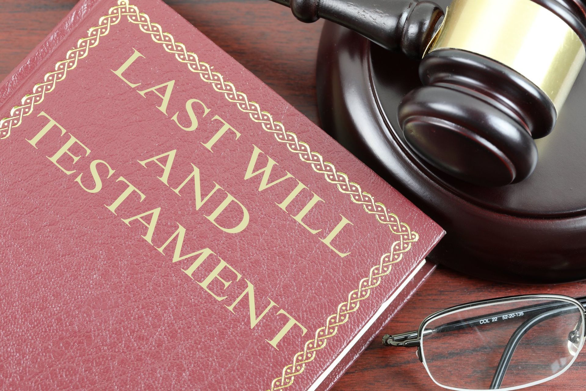 A last will and testament book is sitting on a wooden table next to a judge 's gavel and glasses.