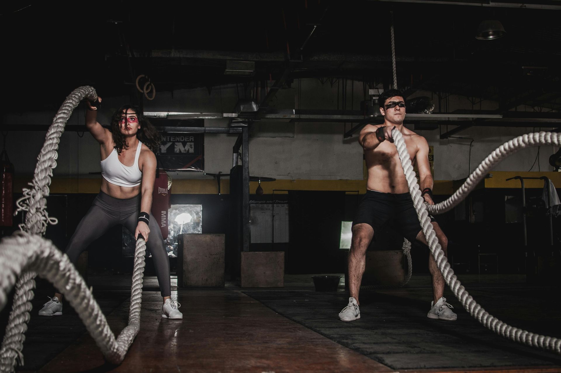 A man and a woman are holding ropes in a gym.