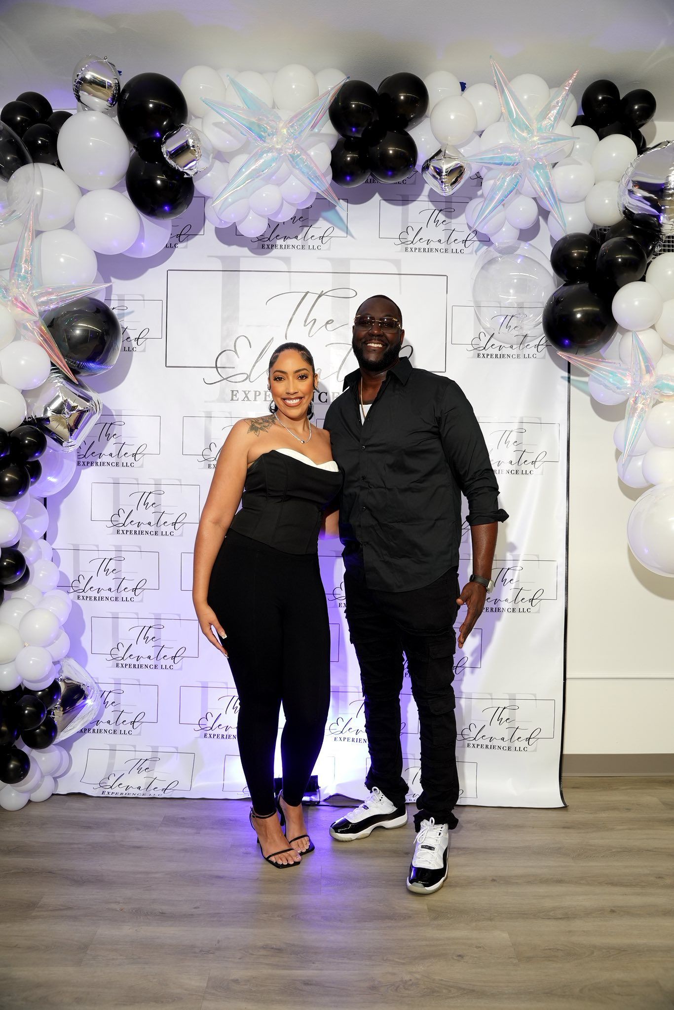 A man and a woman are standing in front of a wall covered in black and white balloons.
