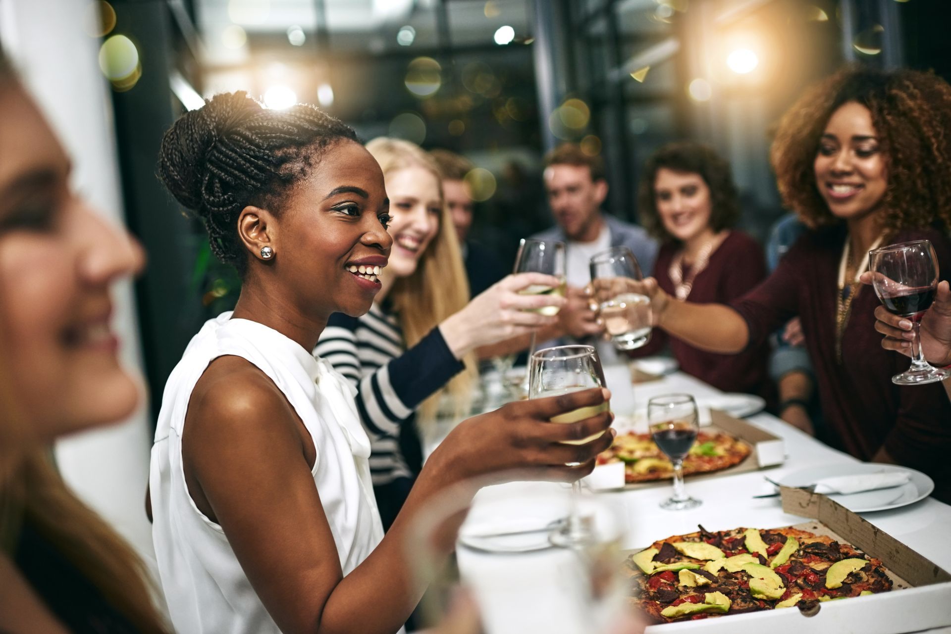 A group of people are sitting at a table eating pizza and drinking wine.