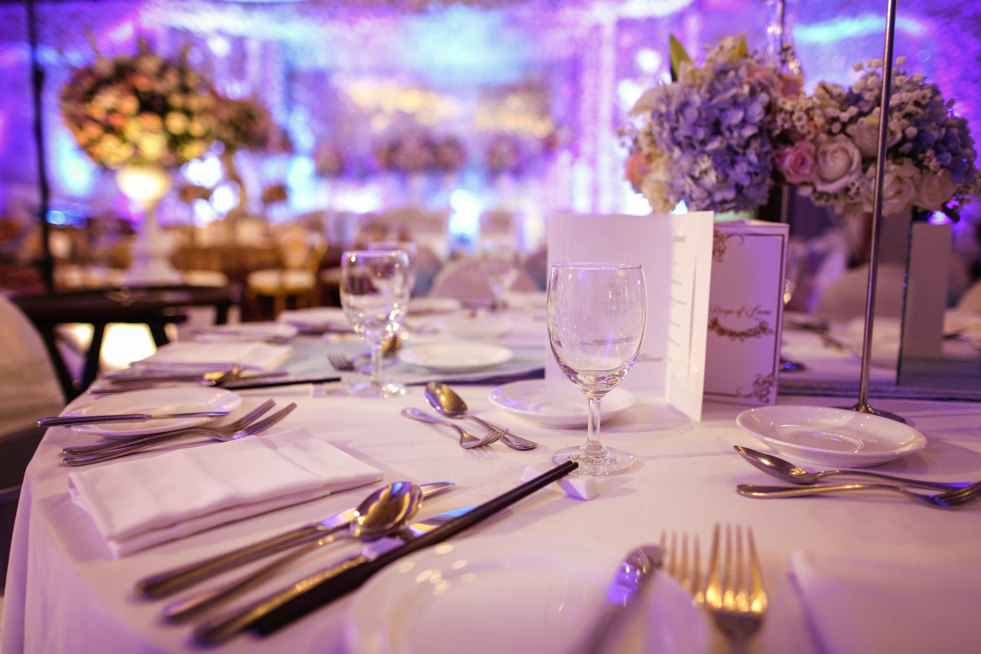 A table set for a wedding reception with plates , utensils , glasses and flowers.