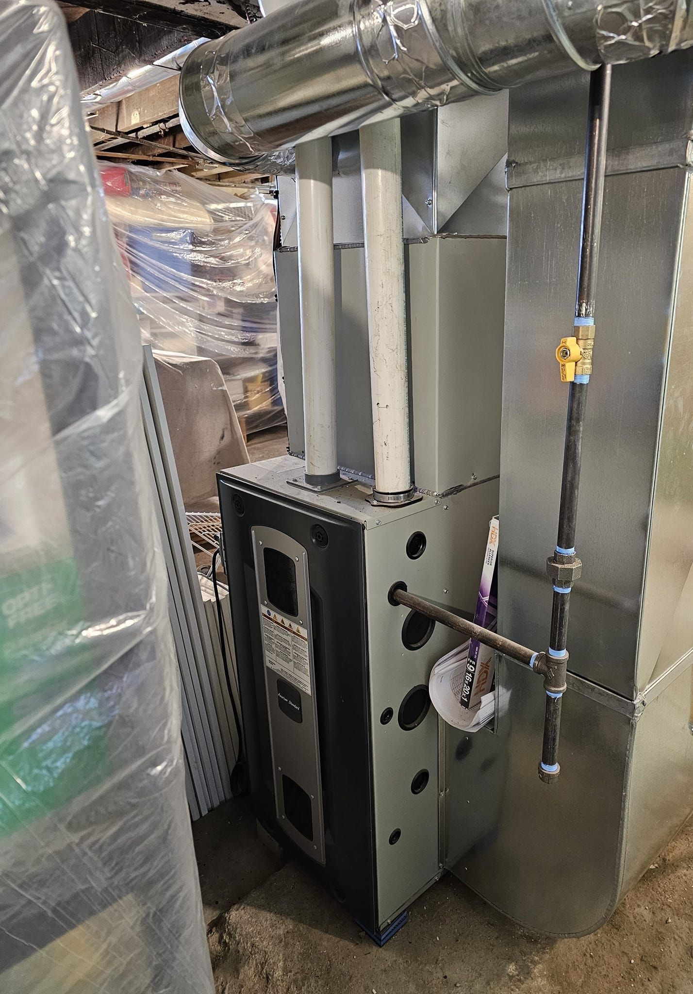 A furnace is sitting in a basement next to a ladder.