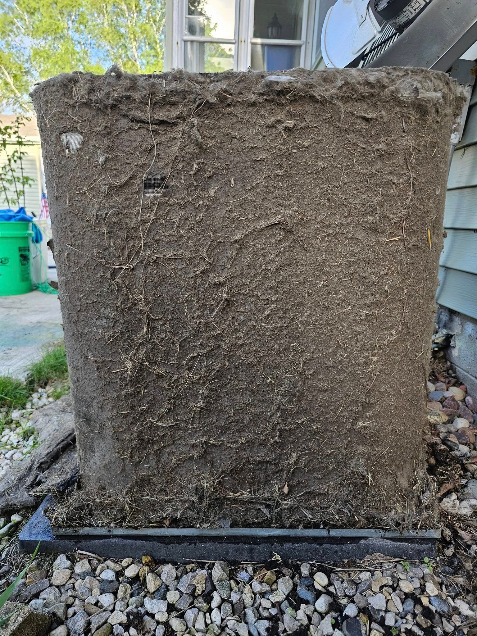 A large concrete pot filled with dirt is sitting on top of a pile of gravel.