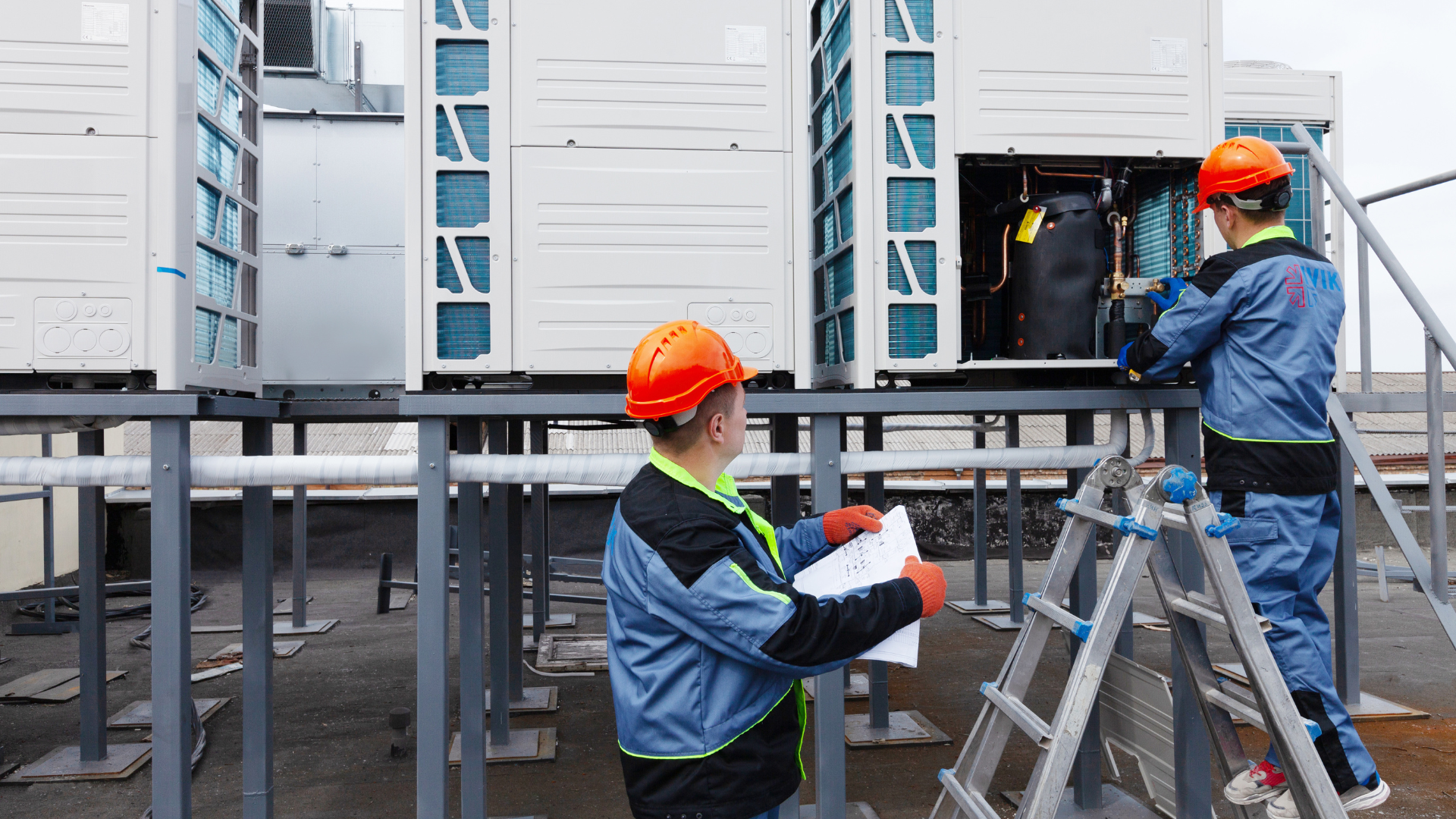 Two men are working on an air conditioner on the roof of a building.