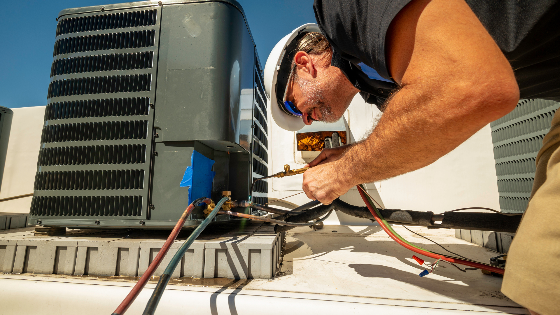 A man is working on an air conditioner on the roof of a building.