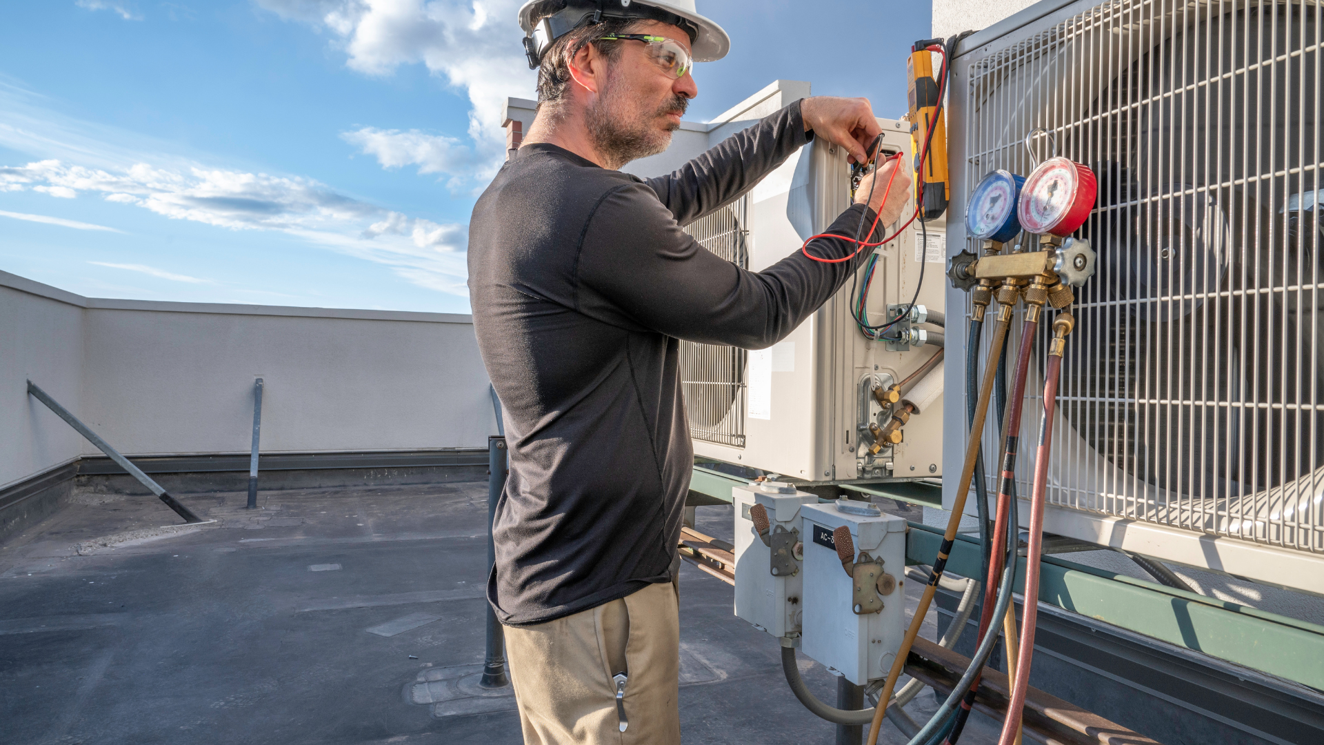 A man is working on an air conditioner on the roof of a building.