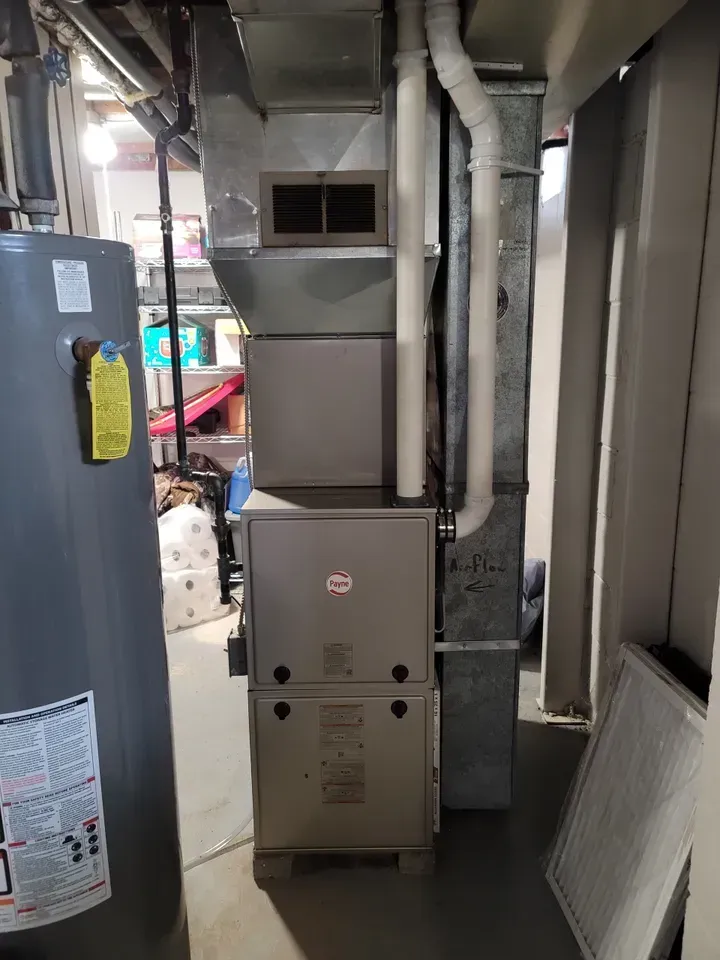 A furnace is sitting in a basement next to a water heater.